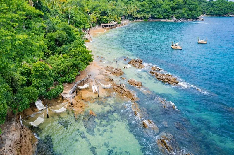 Aerial view of a rocky jungle shoreline with hammocks over the rocks and clear water