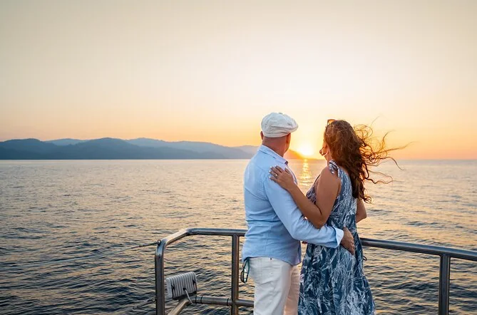 A couple embracing at the rail of a boat as the sun sets over the sea