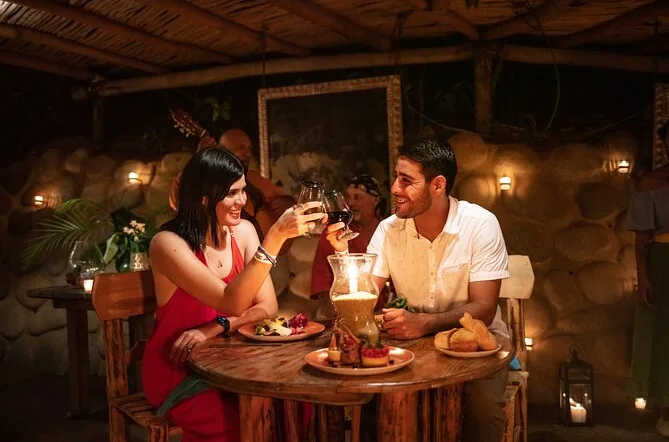 A couple toasting over plates of food at a candlelit wooden table