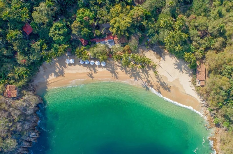 Aerial view of a small horseshoe cove with a sandy beach, umbrellas and turquoise water
